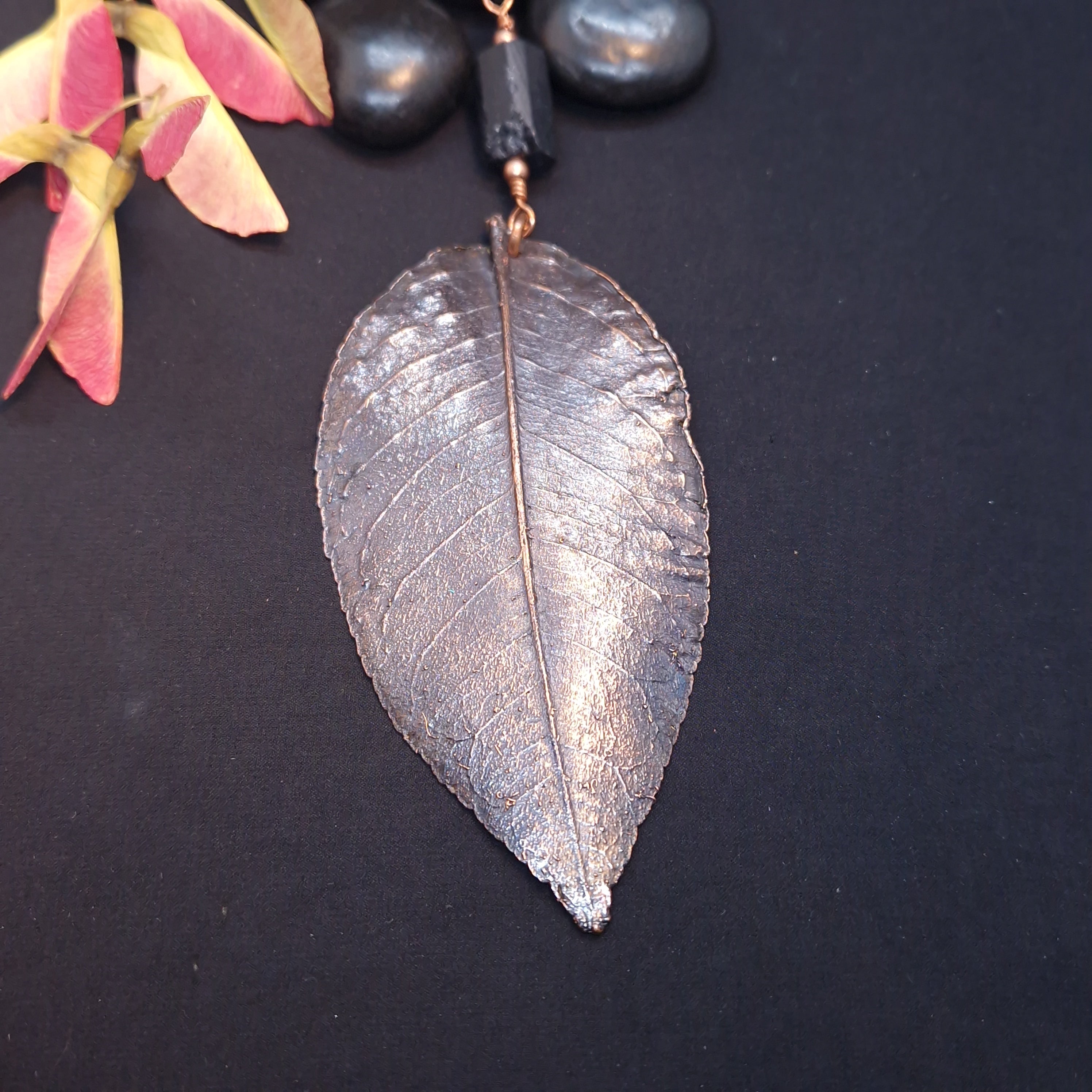 Colgante artesanal de hoja de gardenia electroformada en cobre con pátina envejecida y fluorita negra en bruto, cordón de antelina negra