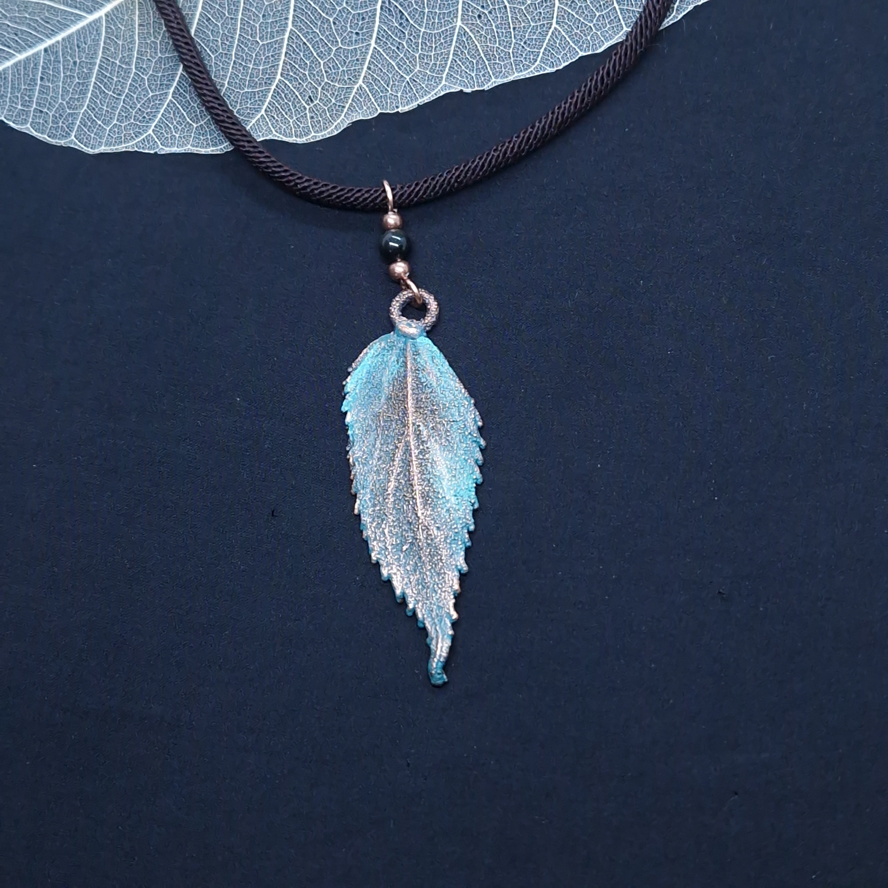 Gargantilla artesanal con hoja de almez electroformada en cobre, bolita de obsidiana negra y cordón marrón, acabado envejecido con pátina verdosa