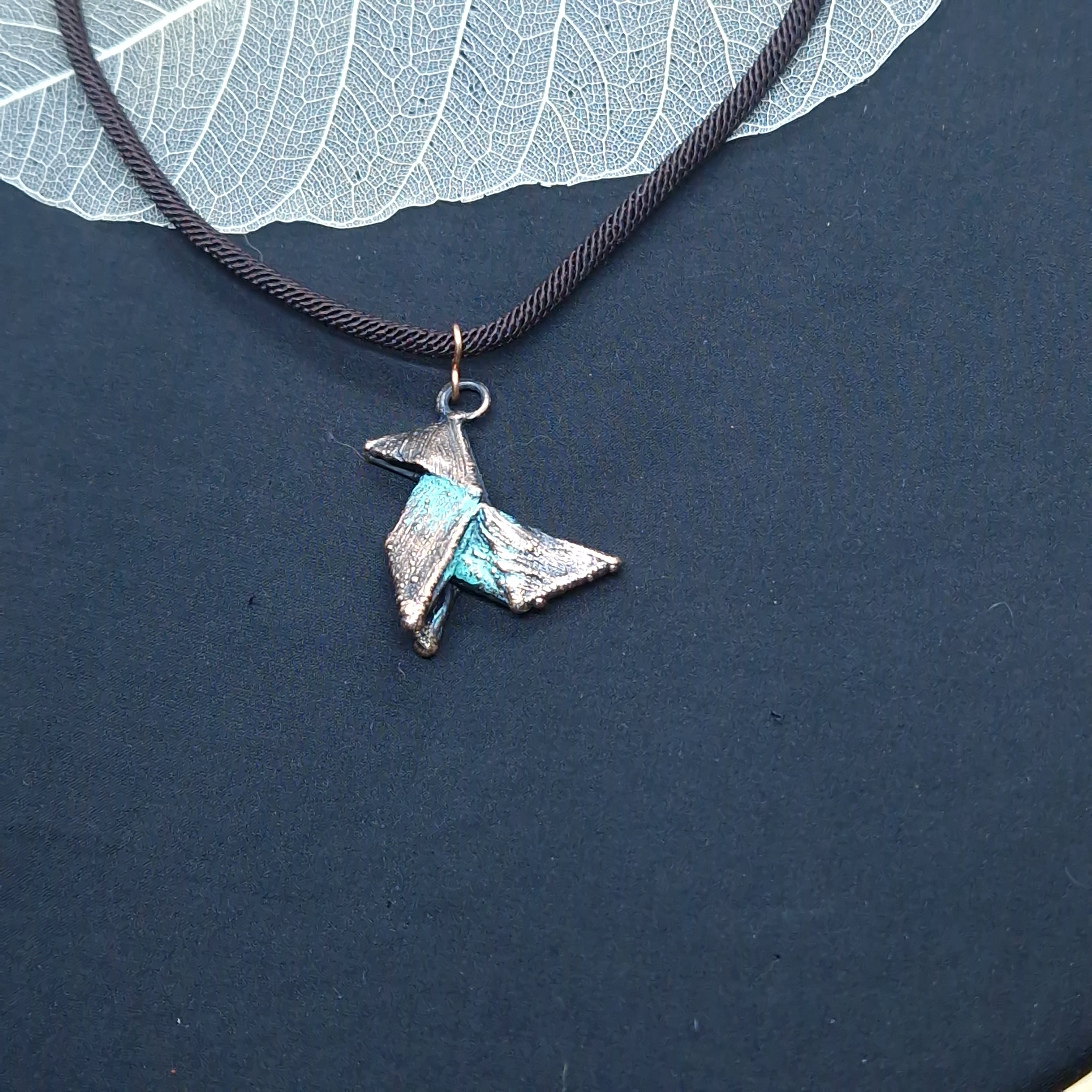 Gargantilla con colgante de pajarita de origami electroformada en cobre con pátina verdosa, sobre cordón marrón trenzado de 40 cm